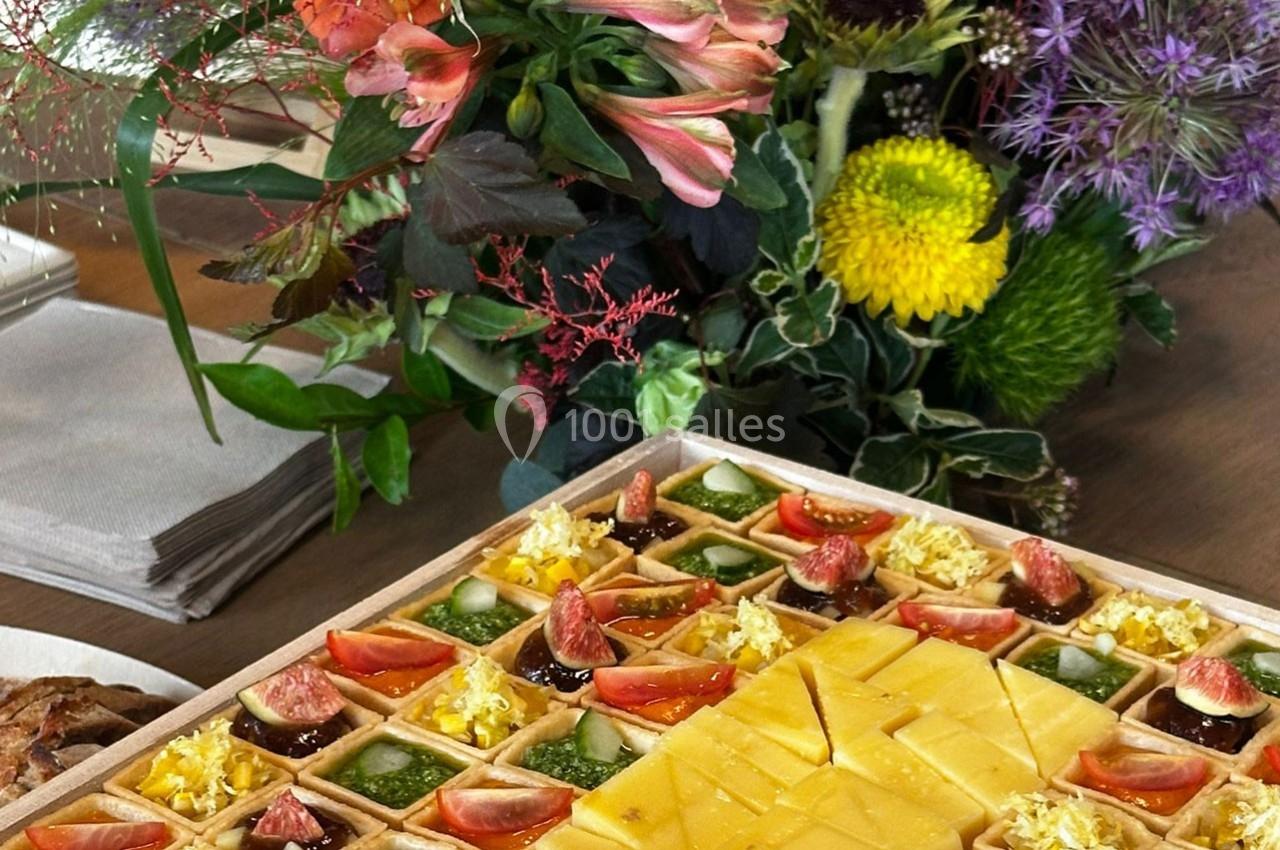 Plateau de bouchées apéritives variées avec fromage, fruits et légumes, accompagné d'un bouquet de fleurs colorées.