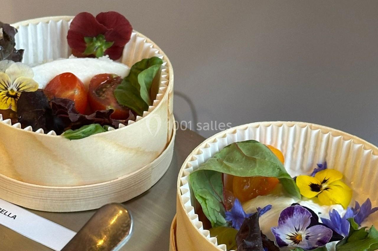 Deux petits plats en bois contenant des légumes frais, des feuilles de salade et des fleurs comestibles colorées.