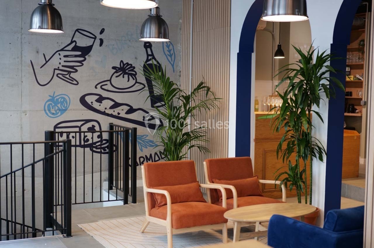 Espace intérieur moderne avec fauteuils orange, table basse en bois, plantes vertes et fresque murale illustrée.