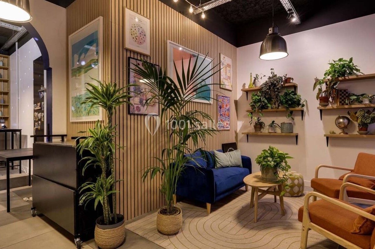 Espace intérieur chaleureux avec plantes, fauteuils colorés, canapé bleu et étagères décorées dans un style moderne.
