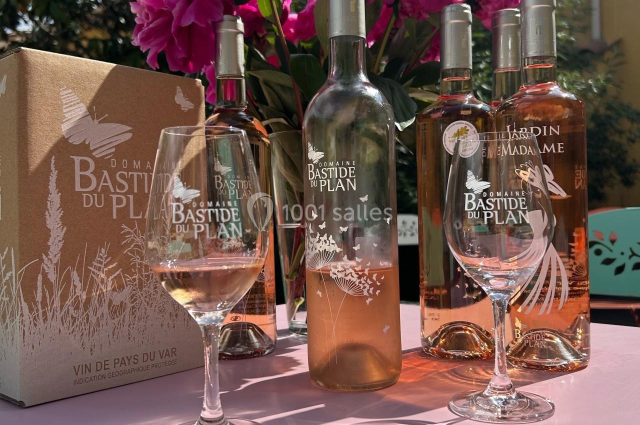 Bouteilles de vin rosé et verres sur une table rose, avec un bouquet de fleurs et une boîte en carton en arrière-plan.