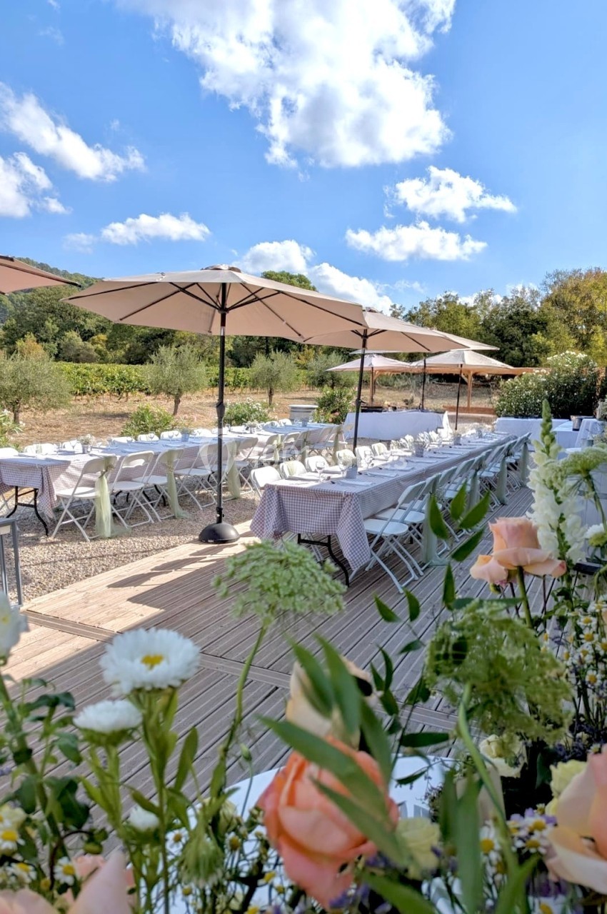 Terrasse extérieure avec tables dressées sous des parasols, entourée de végétation et de fleurs au premier plan.