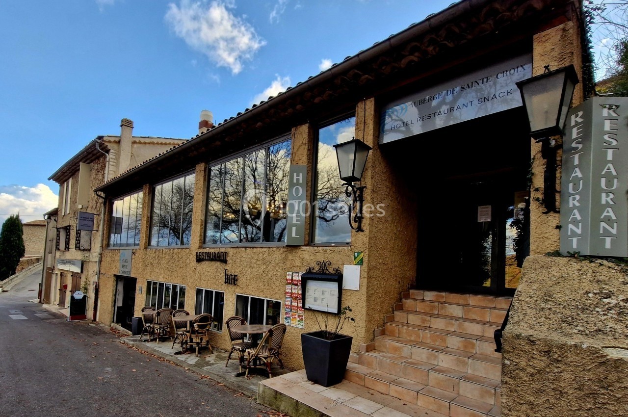 Façade d'un hôtel-restaurant en pierre avec terrasse extérieure, situé le long d'une route calme.