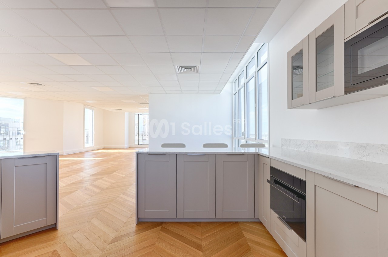 Cuisine moderne lumineuse avec meubles gris, plan de travail en marbre, parquet en bois clair et grandes fenêtres.