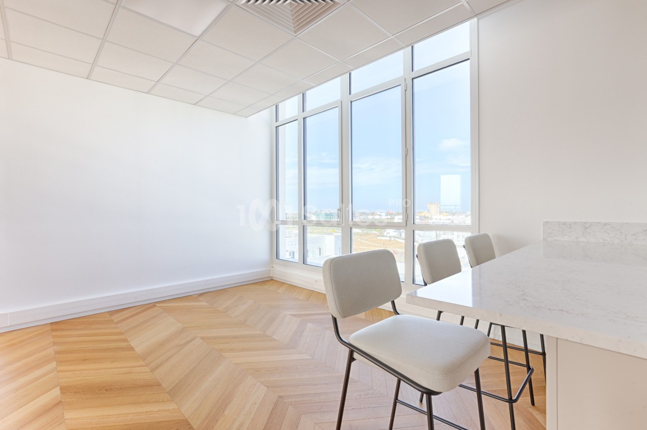 Salle lumineuse avec parquet en chevrons, grandes fenêtres donnant sur une vue dégagée et table avec chaises modernes.