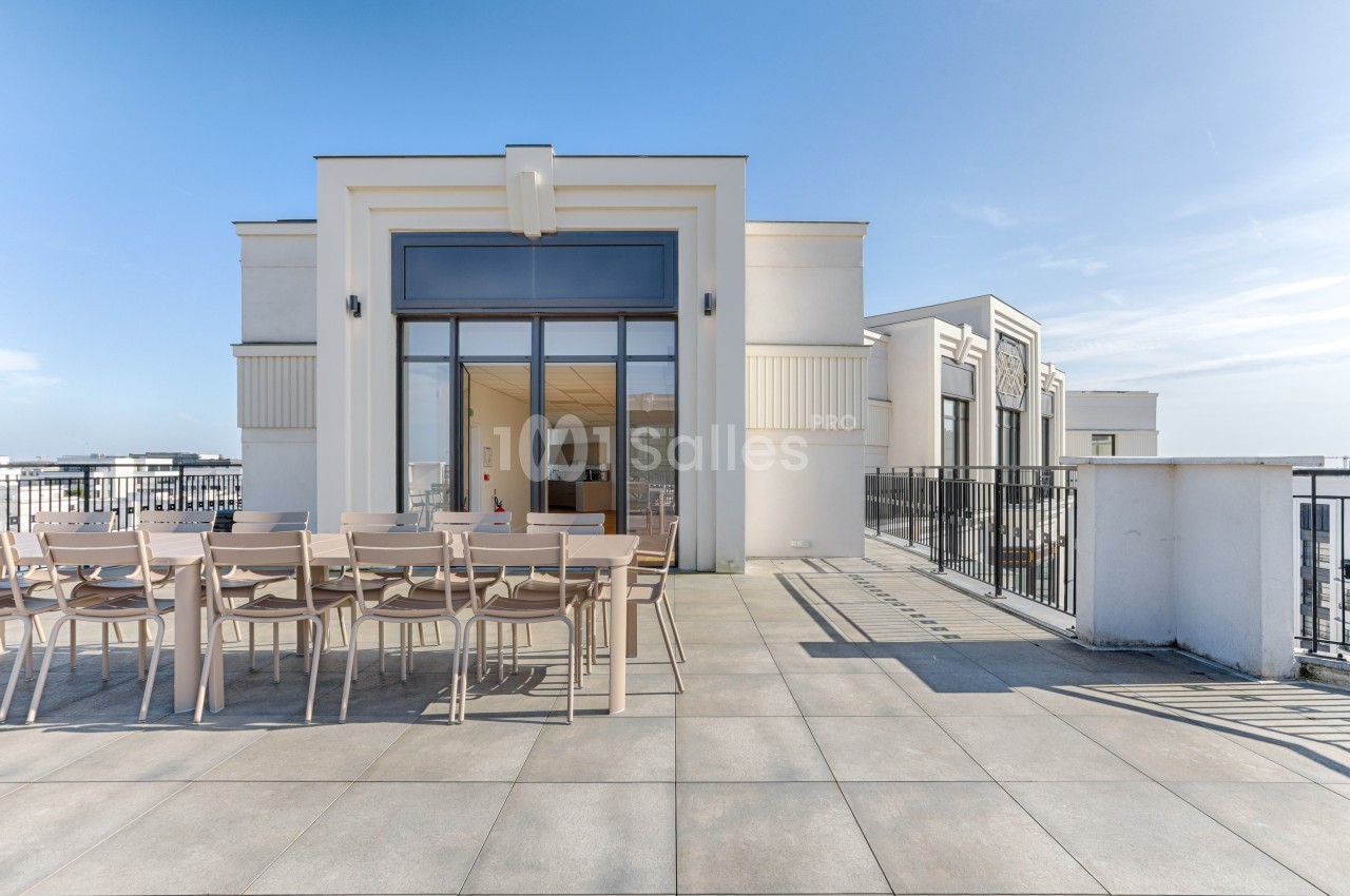 Terrasse spacieuse avec grande table en bois, chaises assorties et vue dégagée sous un ciel bleu.