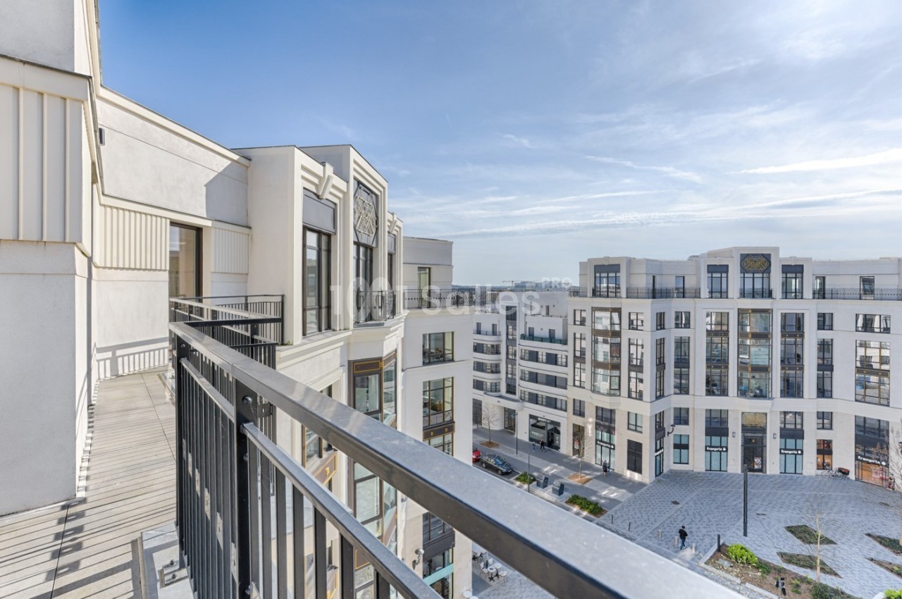 Vue depuis un balcon donnant sur une place entourée d'immeubles modernes sous un ciel dégagé.