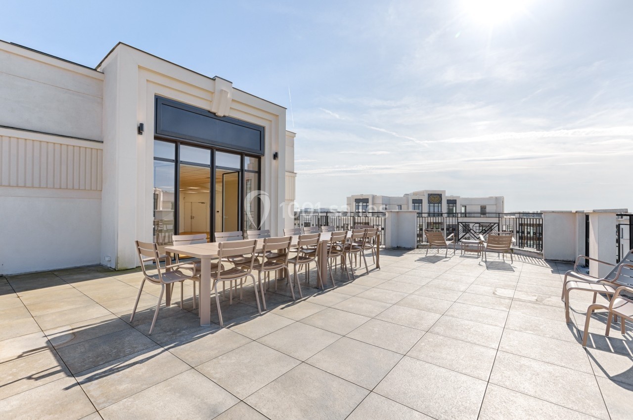Terrasse spacieuse avec mobilier de jardin en bois clair, entourée de garde-corps, sous un ciel ensoleillé.