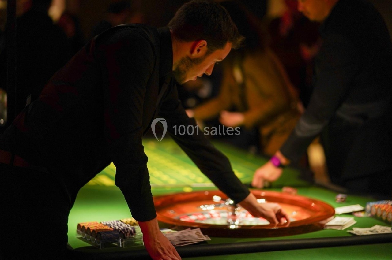 Croupier récupérant des jetons sur une table de roulette dans un casino, avec des joueurs en arrière-plan.