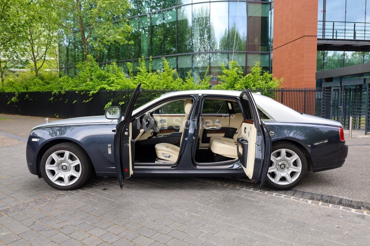 Voiture de luxe grise avec portes ouvertes, intérieur beige, stationnée devant un bâtiment moderne vitré.