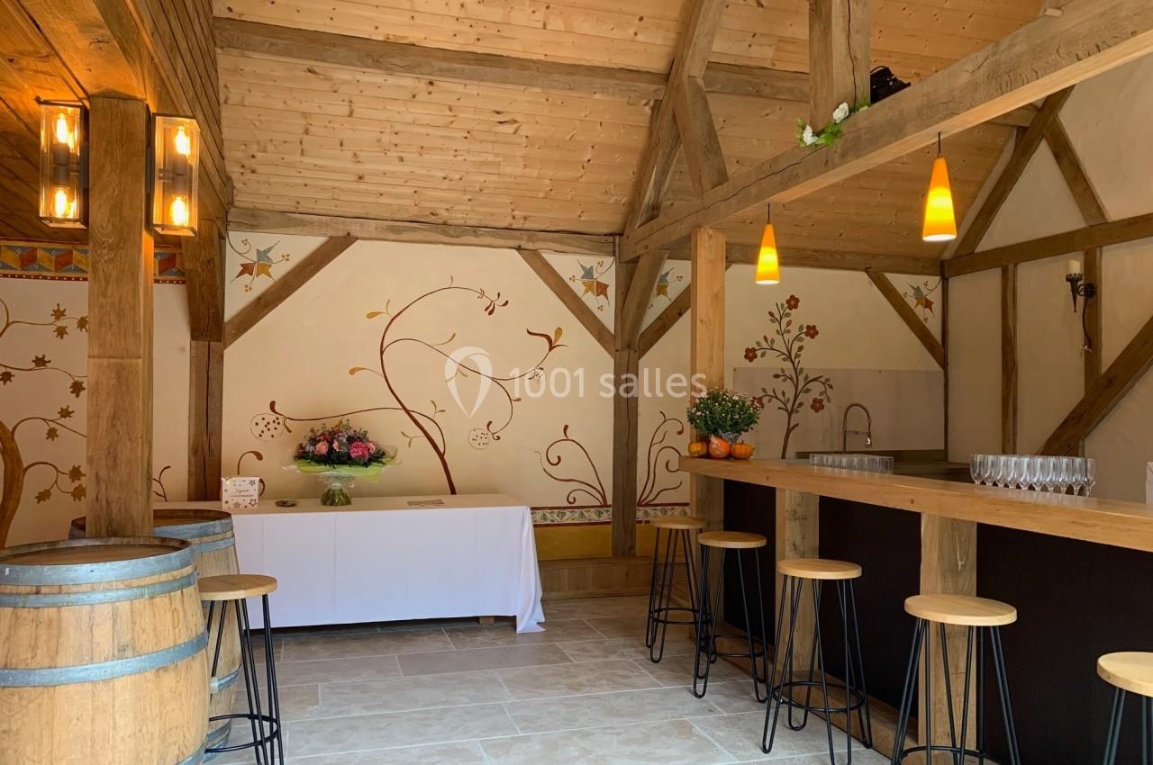 Salle en bois avec un bar, des tabourets, une table décorée de fleurs et des murs ornés de motifs peints.