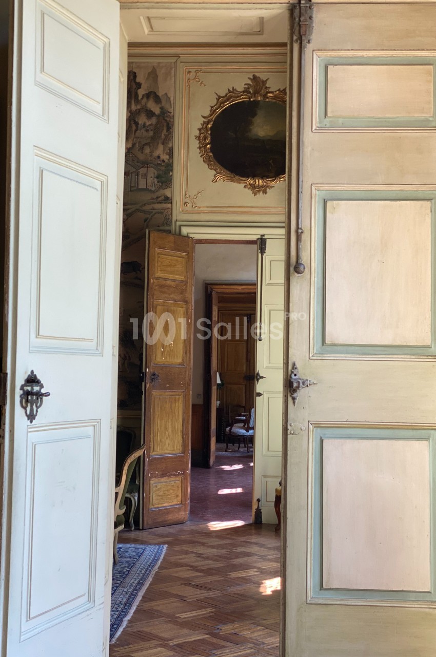 Portes anciennes ouvertes en enfilade révélant un intérieur lumineux avec parquet et décorations murales.