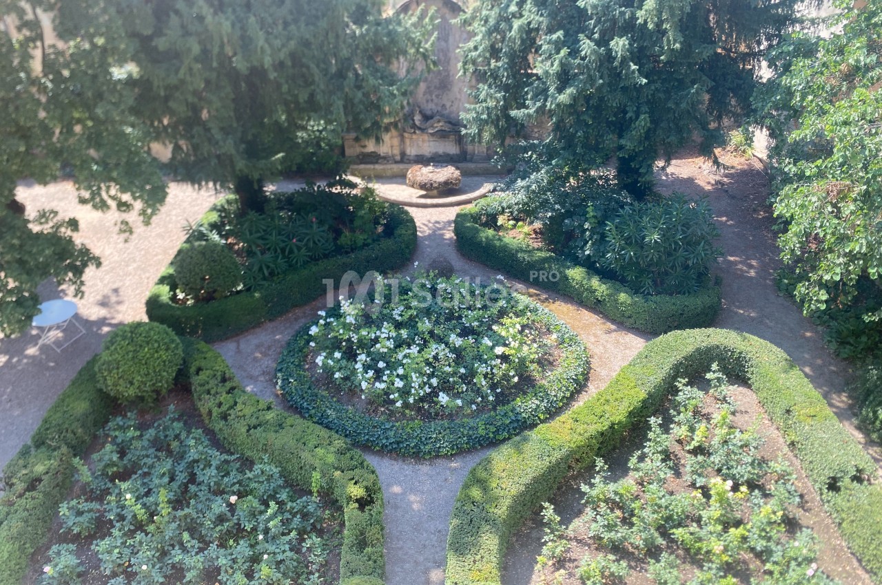 Vue d'un jardin symétrique avec parterres de fleurs, haies taillées et une fontaine en arrière-plan.