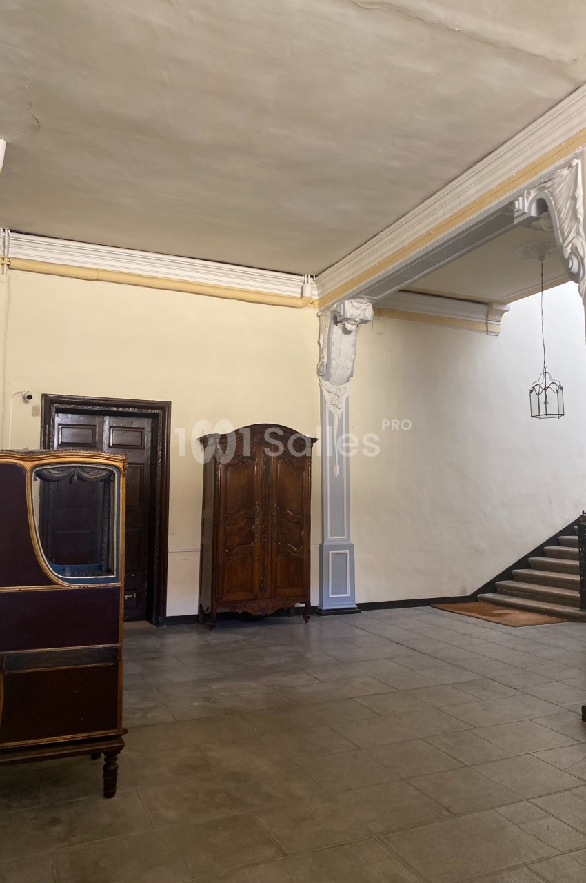 Hall d'entrée avec murs clairs, meubles en bois ancien et escalier montant à droite.