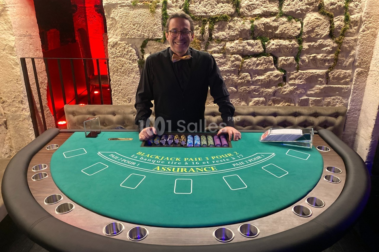 Un croupier souriant se tient derrière une table de blackjack dans un décor en pierre éclairé.