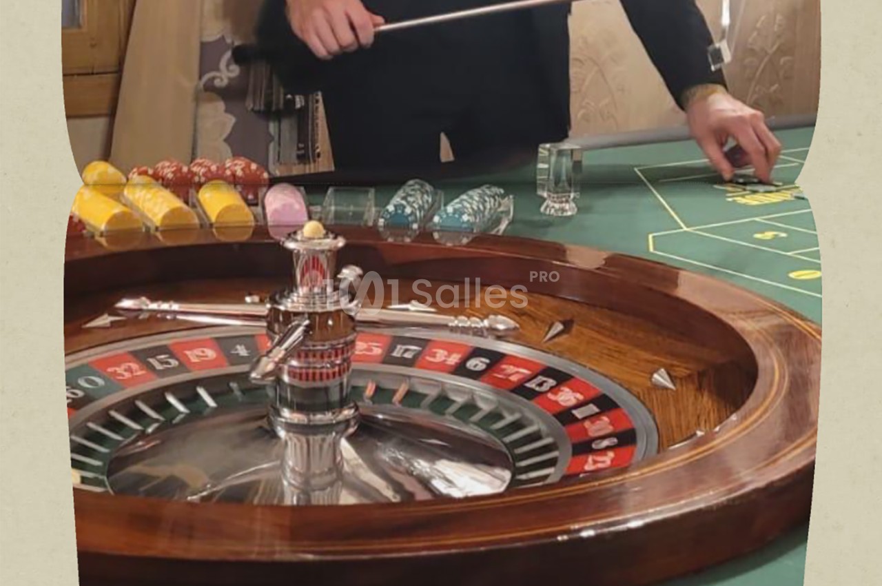 Roulette en bois avec bille en mouvement, jetons colorés et croupier manipulant un râteau sur une table de jeu.