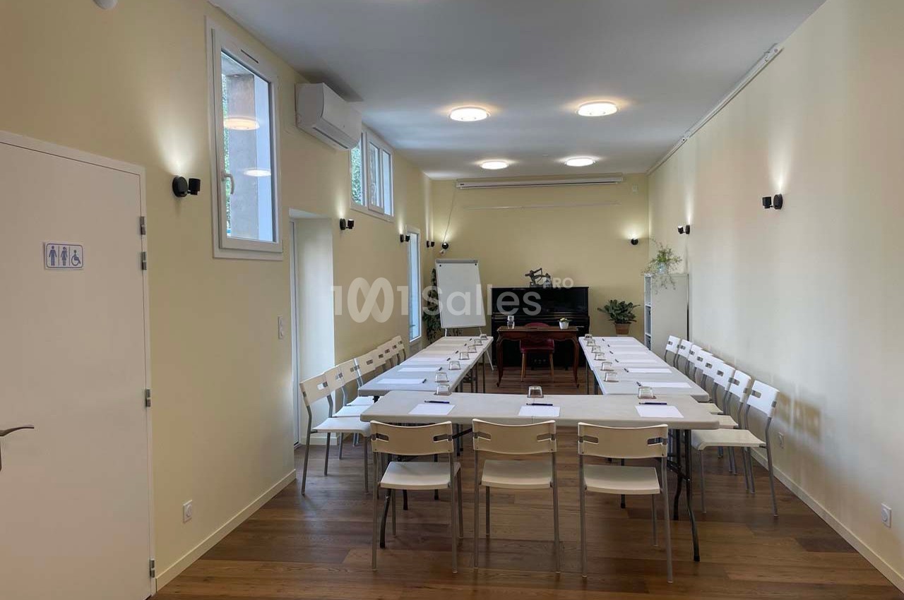 Salle de réunion lumineuse avec des chaises blanches disposées en U autour de tables, tableau blanc en fond.