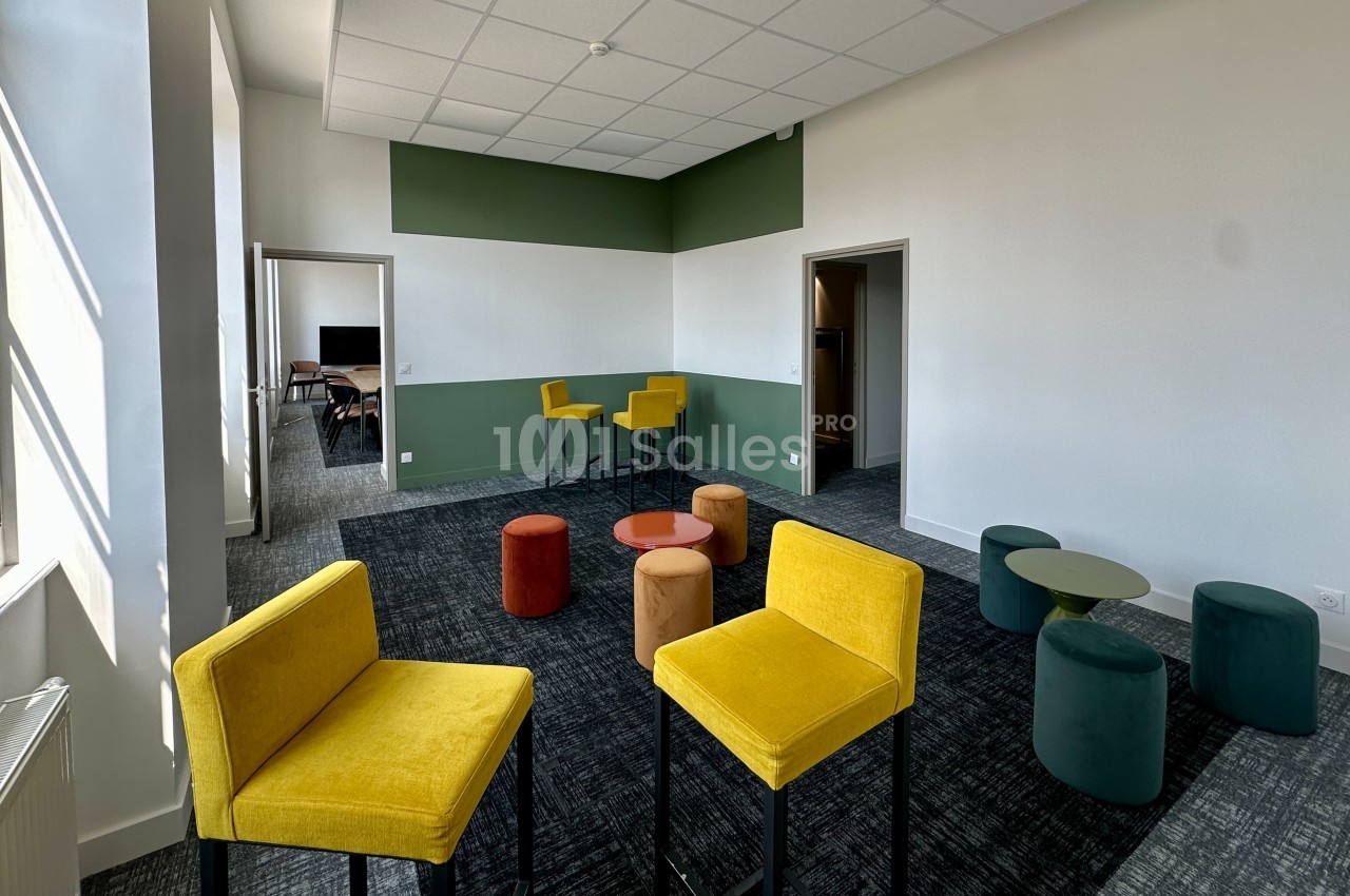 Salle lumineuse avec chaises jaunes, tabourets colorés et tables basses, décorée de murs blancs et verts.