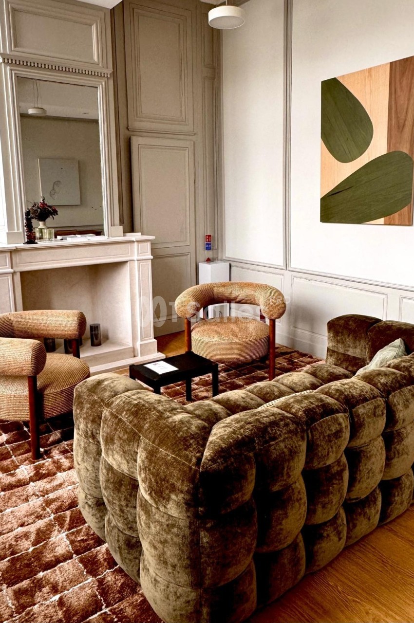Salon élégant avec canapé en velours, fauteuils assortis, cheminée blanche et tableau abstrait sur un mur boisé.