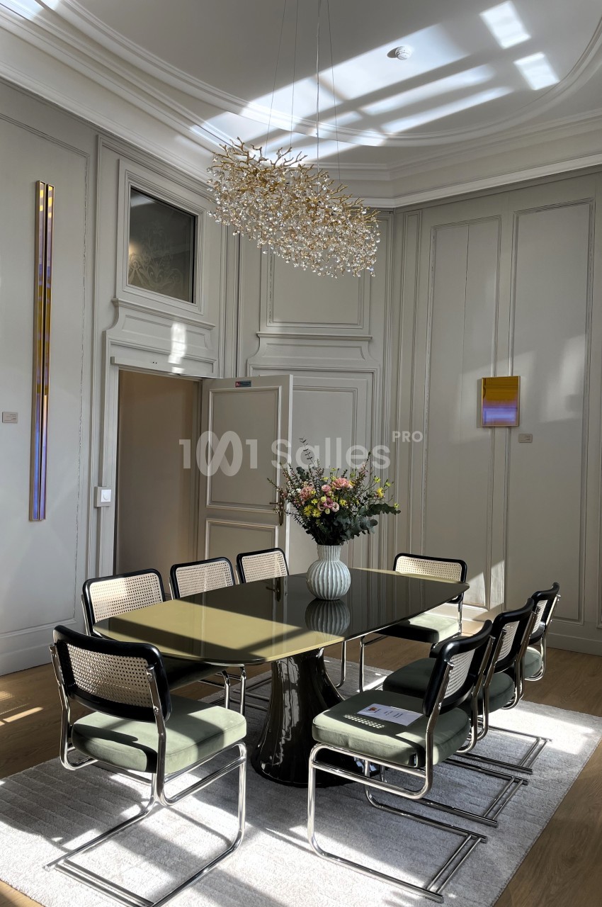 Salle à manger lumineuse avec une table en verre, des chaises modernes, un vase de fleurs et un lustre design.