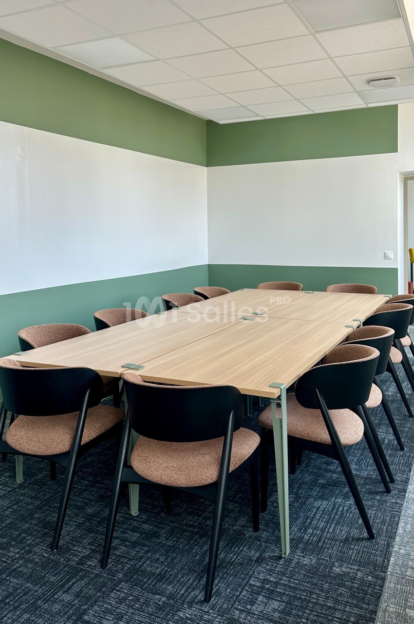 Salle de réunion avec une grande table en bois entourée de chaises, éclairée par une lumière naturelle.