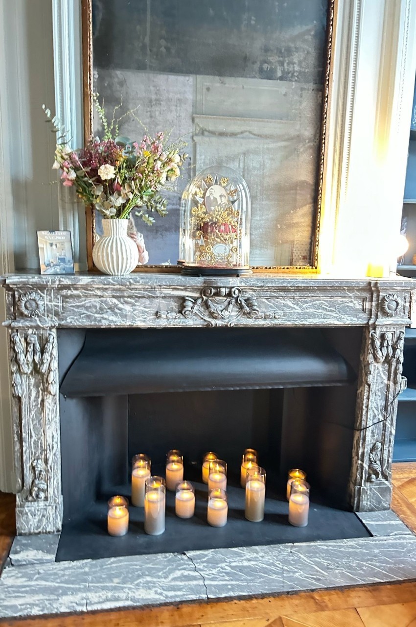 Cheminée en marbre gris décorée de bougies allumées, d'un bouquet de fleurs et d'une cloche en verre.