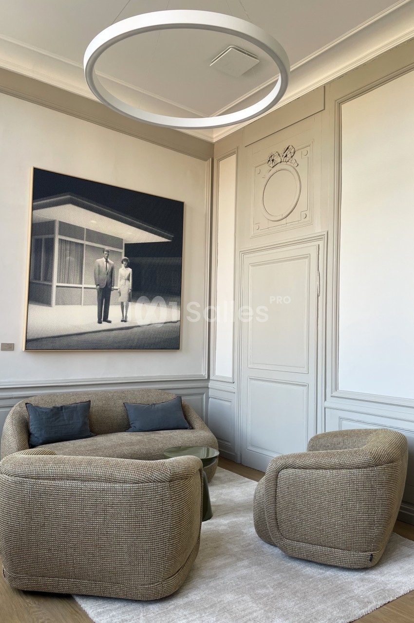 Salon lumineux avec deux fauteuils et un canapé beige sur un tapis clair, décoré d'un tableau moderne et d'un luminaire…