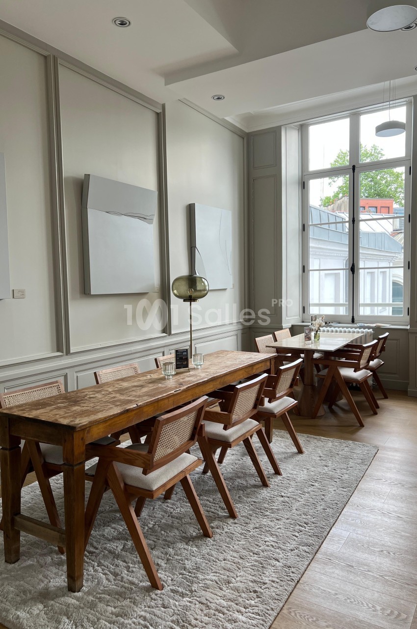 Salle à manger lumineuse avec table en bois, chaises en rotin, tapis clair et grande fenêtre donnant sur l'extérieur.