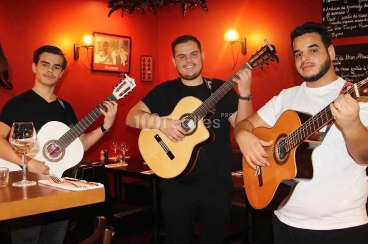 Trois musiciens jouent de la guitare dans un restaurant à l'ambiance chaleureuse avec des murs rouges.