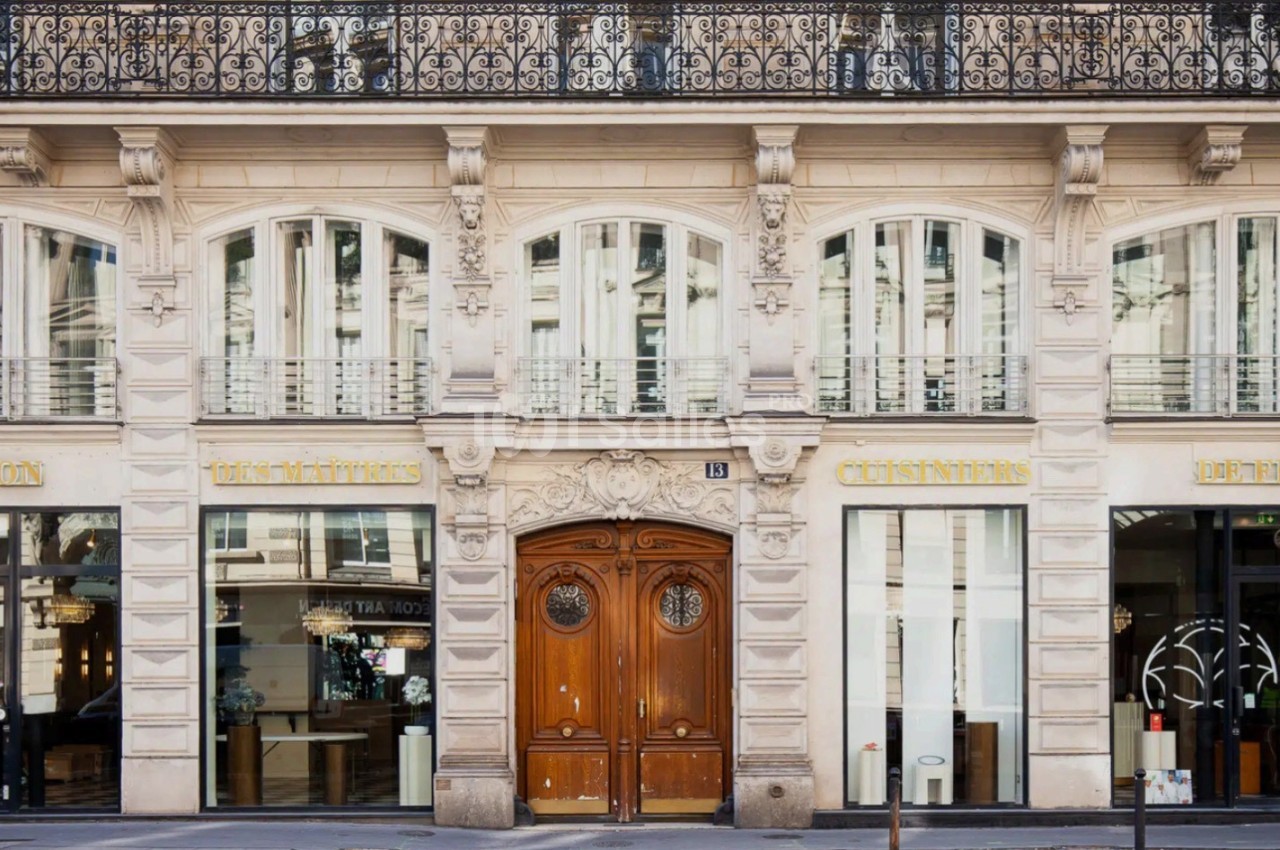 Façade d'un immeuble haussmannien avec une porte en bois centrale et des vitrines commerciales de part et d'autre.