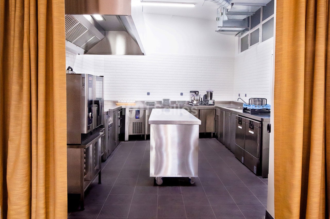 Cuisine professionnelle équipée avec plan de travail en inox, appareils de cuisson et murs carrelés blancs.