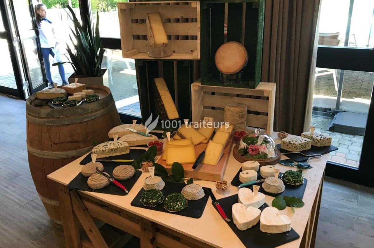 Plateau de fromages variés disposés sur une table, avec des caisses en bois et un tonneau en arrière-plan.