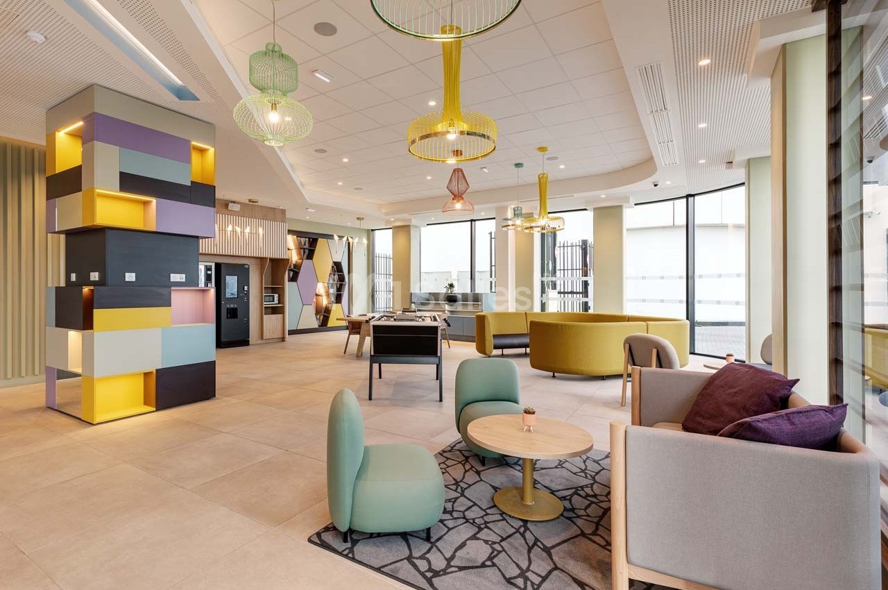 Espace intérieur lumineux avec mobilier moderne, coin salon, tables, et grandes fenêtres laissant entrer la lumière…