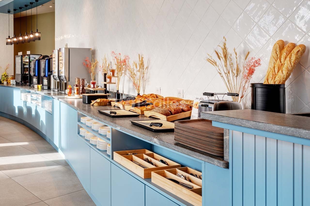 Buffet de petit-déjeuner avec viennoiseries, pains, boissons chaudes et couverts disposés sur un comptoir bleu.