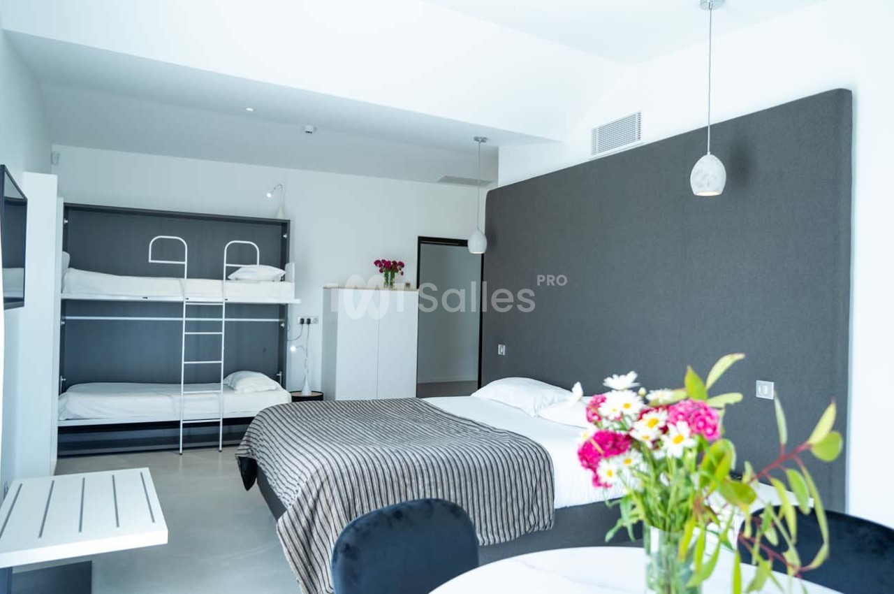 Chambre lumineuse avec un lit double, des lits superposés, une table avec fleurs et un décor moderne minimaliste.