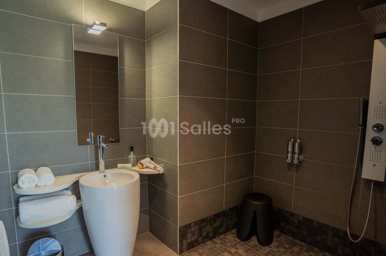 Salle de bain moderne avec lavabo sur pied, miroir éclairé, douche à jets et carrelage gris foncé.