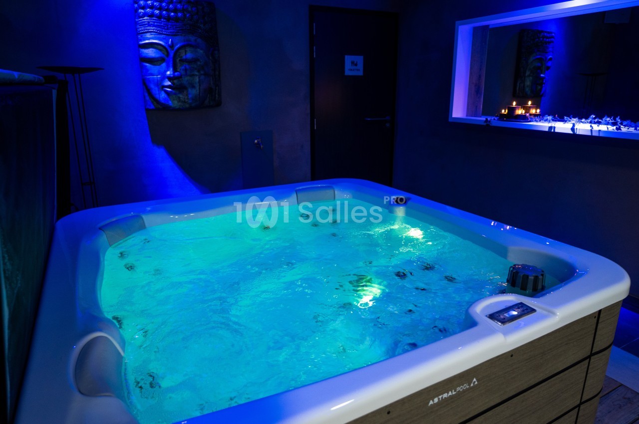 Bain à remous éclairé dans une pièce sombre avec une décoration murale et une ambiance relaxante.