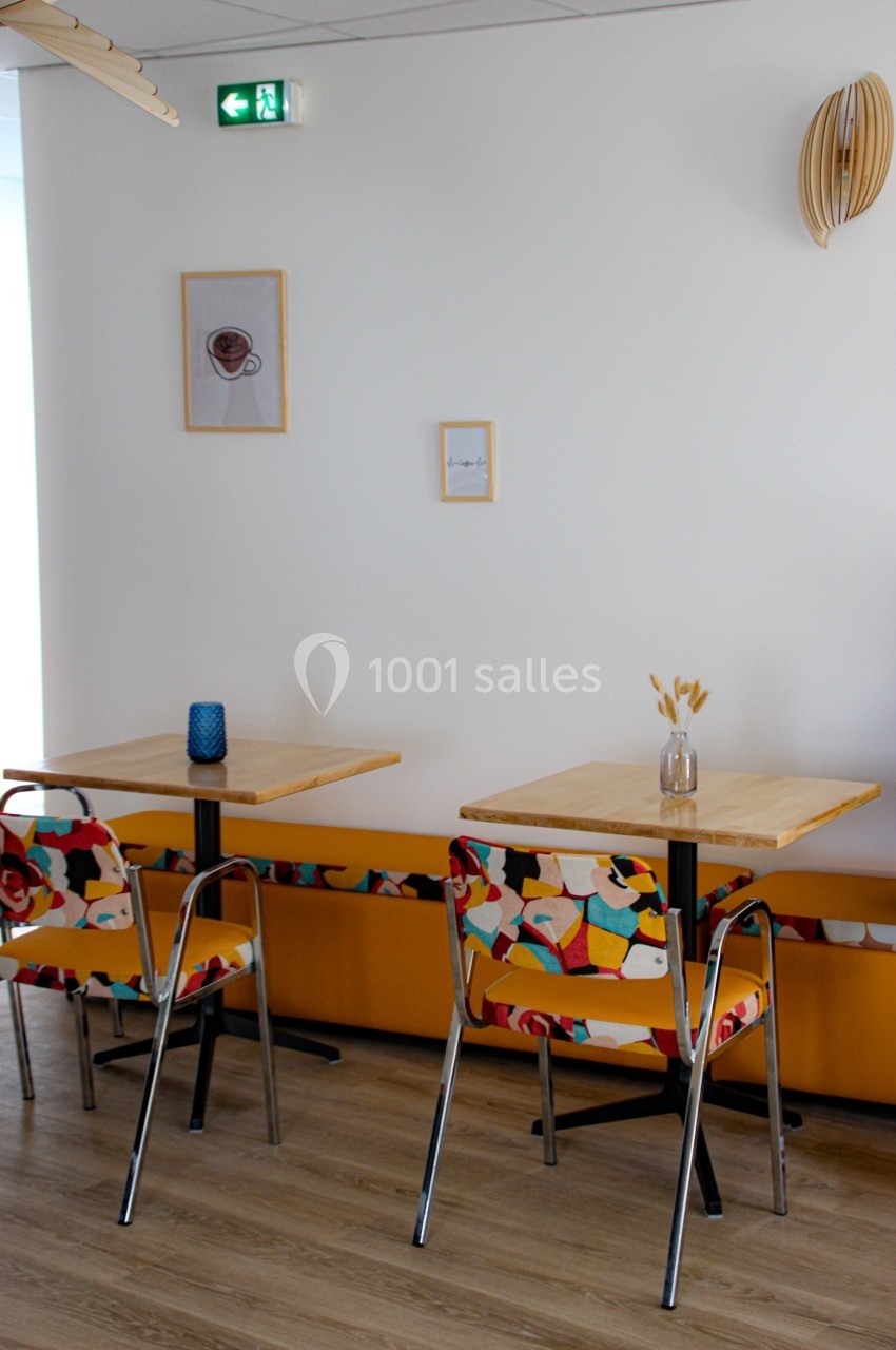 Deux tables avec chaises colorées dans un espace lumineux, décoré de cadres et d'éléments en bois.