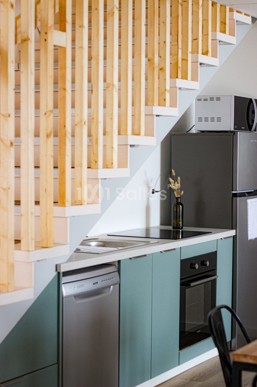 Cuisine compacte sous un escalier en bois, équipée d'un four, d'un lave-vaisselle, d'un réfrigérateur et d'un plan de…