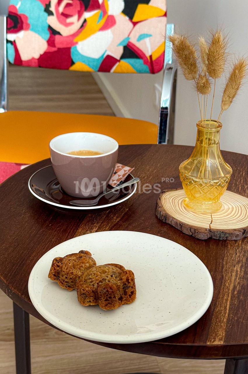 Tasse de café avec une assiette de petits gâteaux sur une table en bois, décorée d'un vase et d'une chaise colorée en…