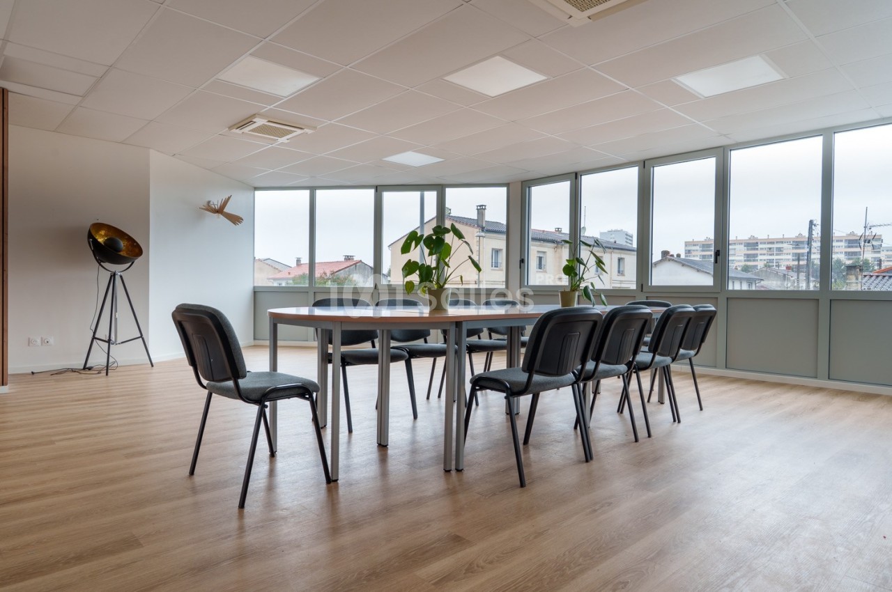 Salle de réunion lumineuse avec table rectangulaire, chaises noires, sol en bois et grandes fenêtres donnant sur des…
