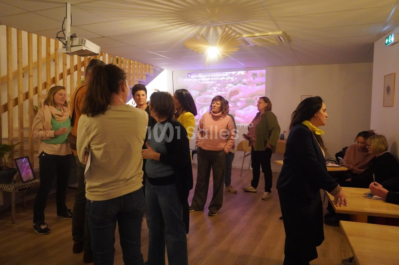 Des personnes discutent dans une salle lumineuse avec un projecteur affichant une image en arrière-plan.