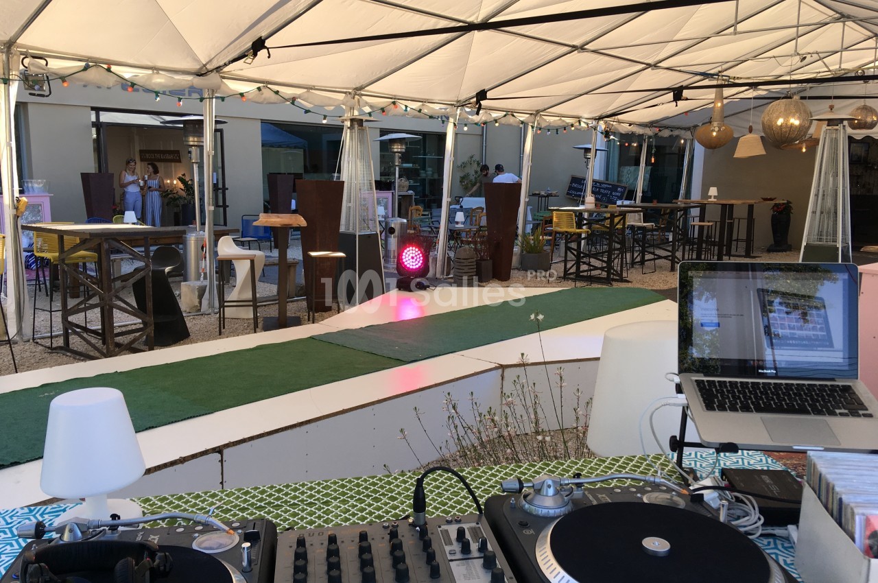 Terrasse couverte avec piste de danse, tables hautes, décoration lumineuse et équipement de DJ au premier plan.