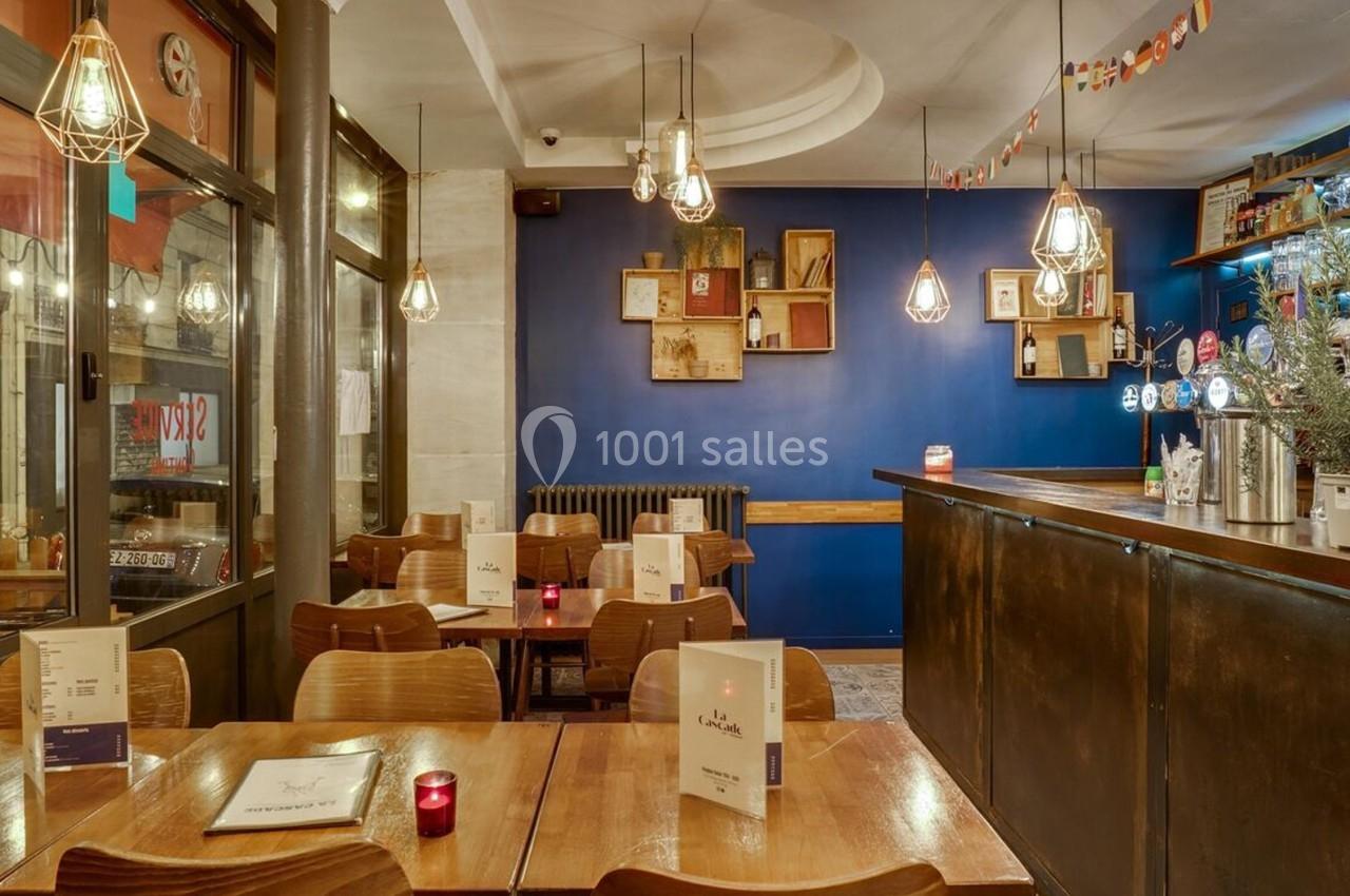 Salle de restaurant chaleureuse avec tables en bois, éclairage suspendu et décoration murale moderne.