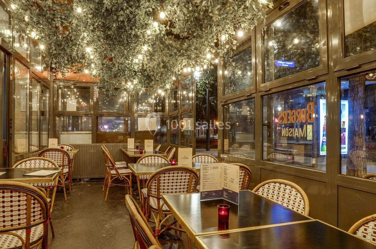 Salle de restaurant avec des tables en rotin, éclairage chaleureux et plafond décoré de feuillage et guirlandes lumineuses.