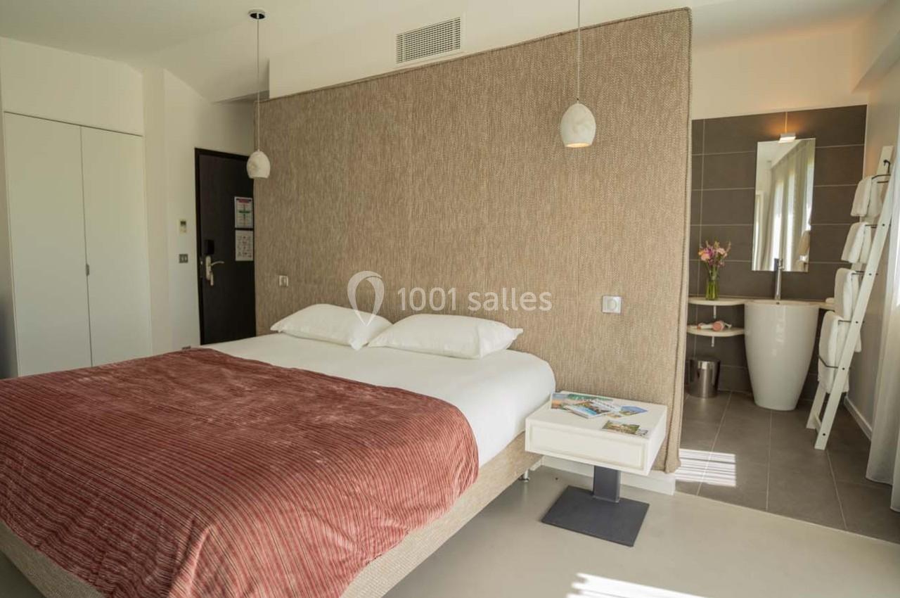 Chambre lumineuse avec lit double, mur en tissu beige, salle de bain attenante et décoration épurée.