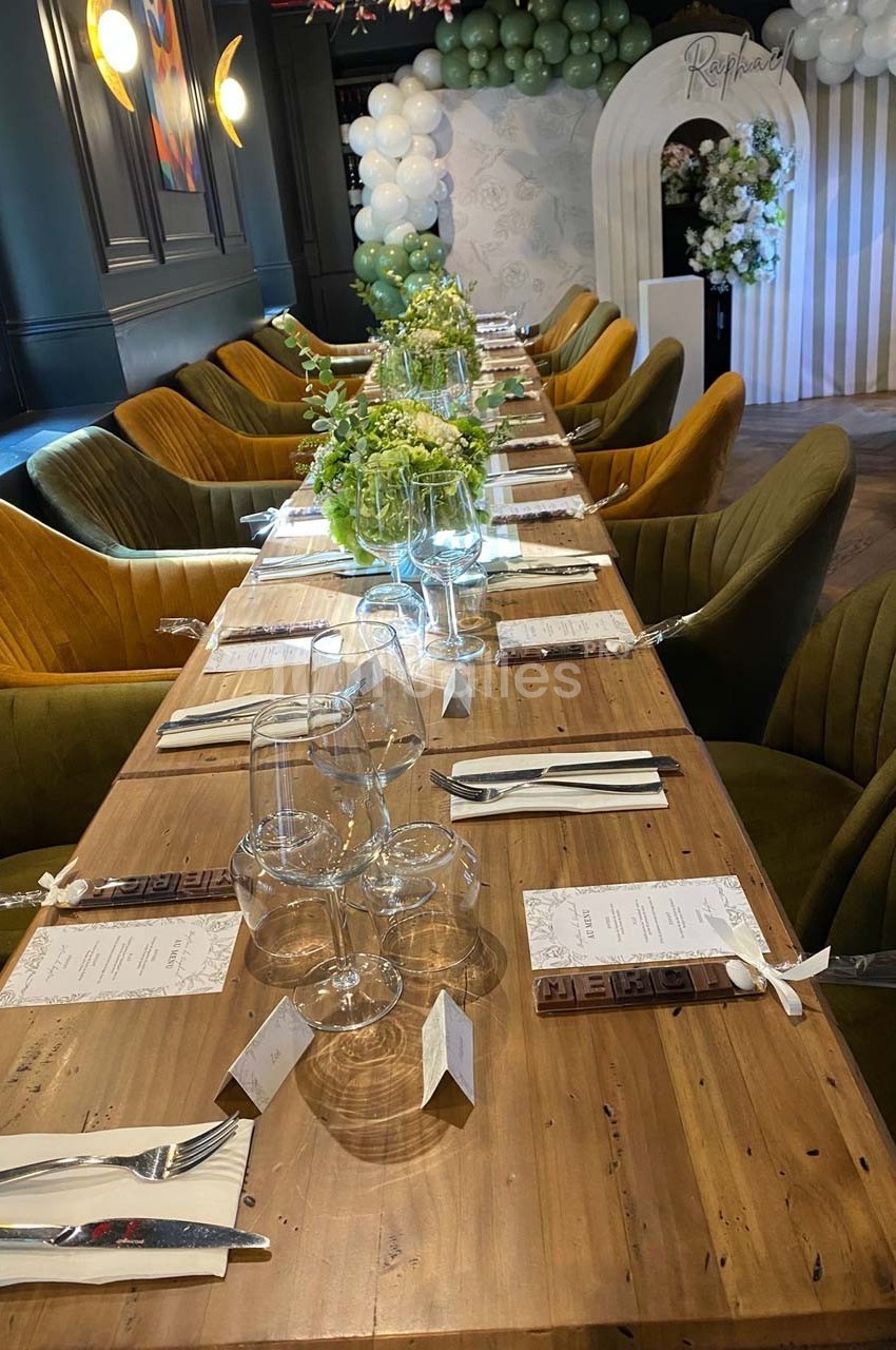 Table en bois dressée pour un repas, avec verres, couverts, menus et décorations florales, dans une salle élégante.