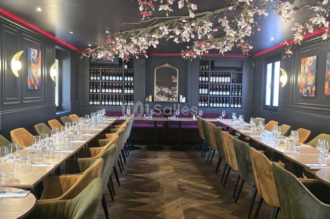 Salle de restaurant élégante avec tables dressées, chaises en velours, éclairage doux et décoration florale suspendue.