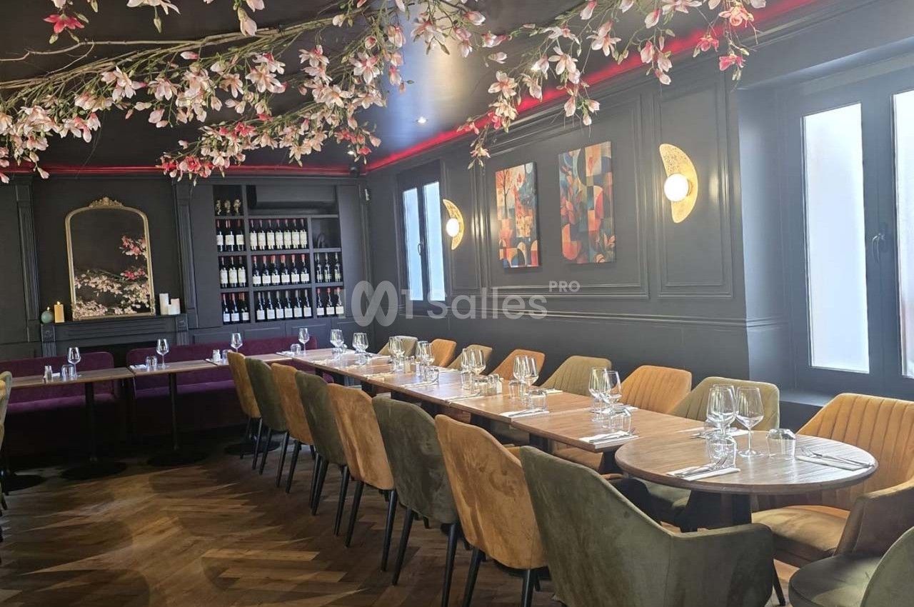 Salle de restaurant élégante avec une longue table en bois, chaises colorées et décoration florale suspendue.