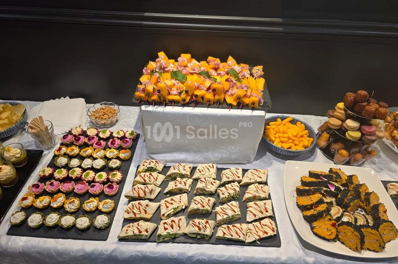 Buffet de desserts variés comprenant gâteaux, cupcakes, brochettes de fruits et macarons disposés sur une table blanche.